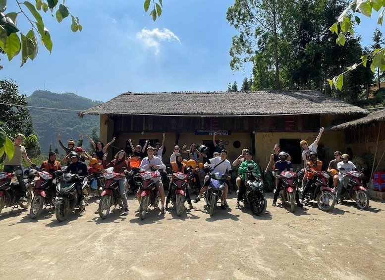A group of people on motorcycles in front of a rustic building with a thatched roof. 3
