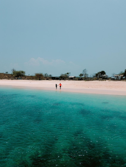 A beach with clear turquoise water and a person walking on the shore. 1