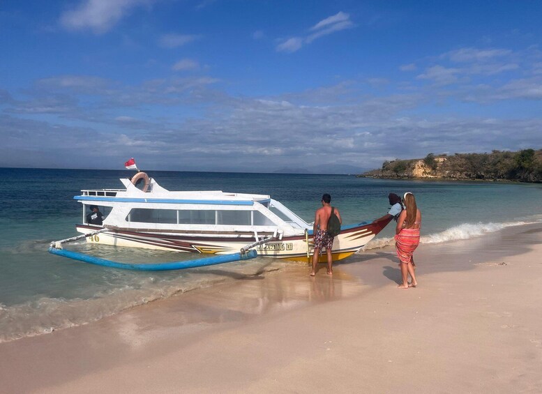 A boat on a sandy beach with clear blue water and a rocky island in the background. 1