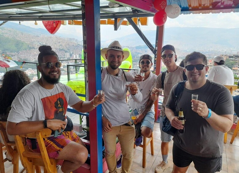 A group of people sitting and standing at a rooftop bar with a cityscape in the background. 2