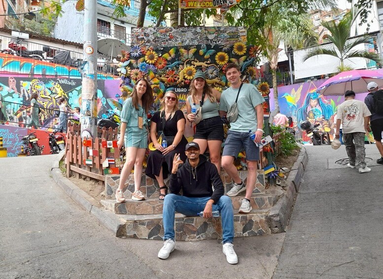 A group of people posing in front of a colorful mural with sunflowers and other designs. 5