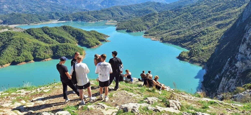 A group of people on a mountain trail overlooking a turquoise lake surrounded by lush greenery. 2