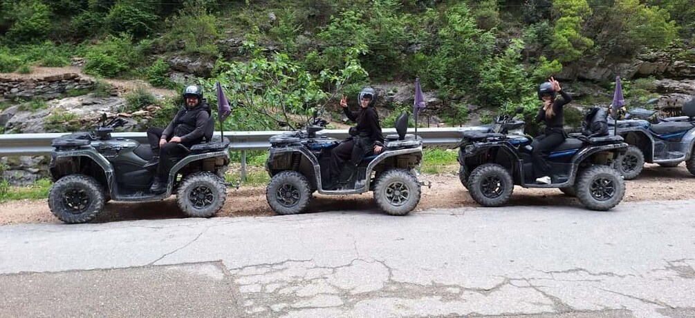 Three people on ATVs on a road with greenery in the background. 3