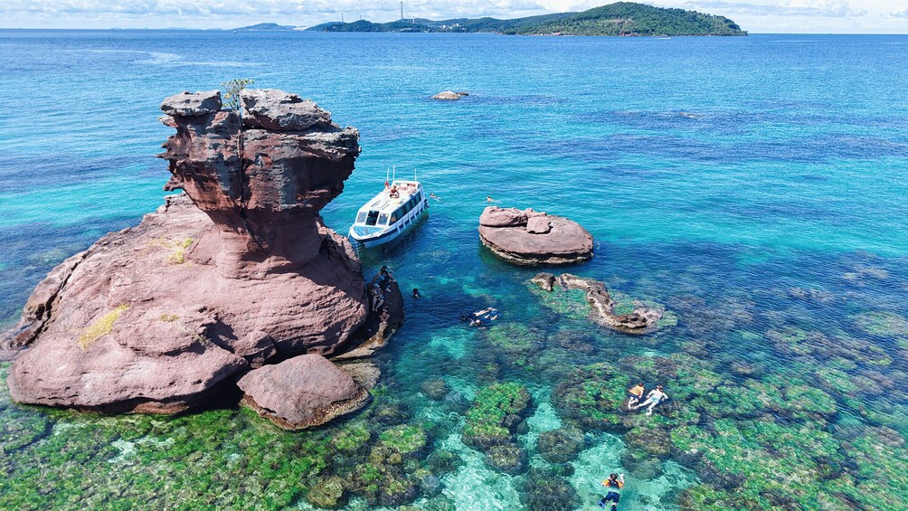 A boat near rocky formations in clear blue waters with people snorkeling. 1