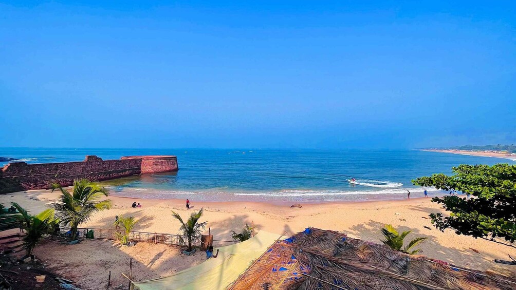 A beach with palm trees, a sandy shore, and a large brick structure in the water. 1