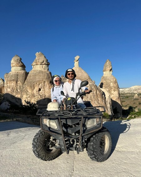 Two people on an ATV in front of rock formations. 1