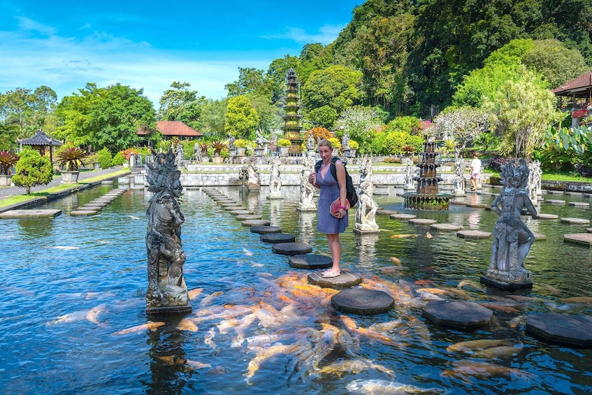 A woman standing on stepping stones over a koi pond with fish, surrounded by statues and a pagoda. 5