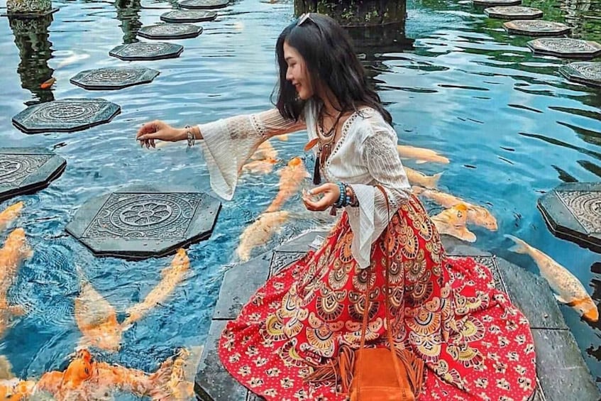 A person in a patterned dress reaching towards koi fish in a pond with patterned stepping stones. 3