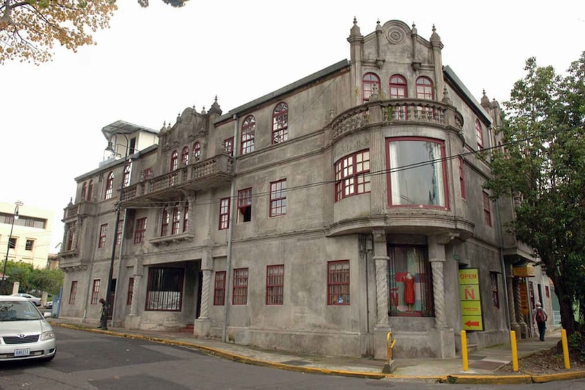A historic building with ornate architecture, a large window with a red curtain, and a sign indicating an open entrance. 2