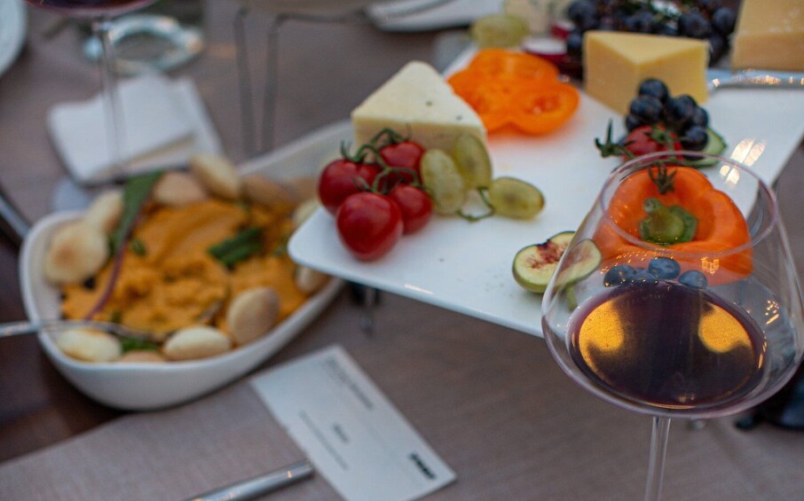 A table with a variety of foods including cheese, tomatoes, grapes, and a bowl of dip. 3