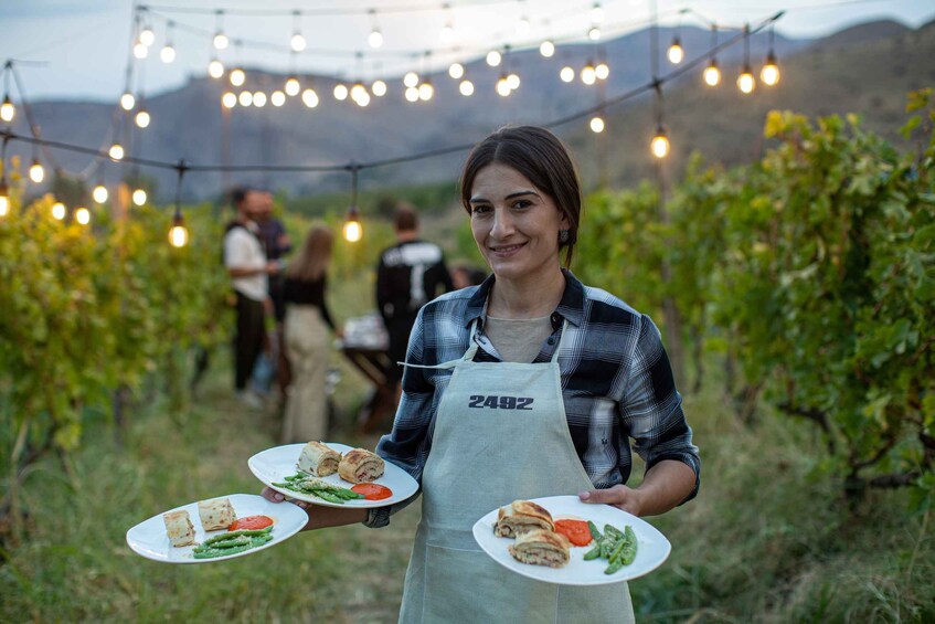 A person holding plates with food in an outdoor setting with string lights. 5