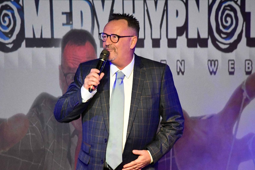 A person in a blue checkered suit and light blue tie speaking into a microphone. 3