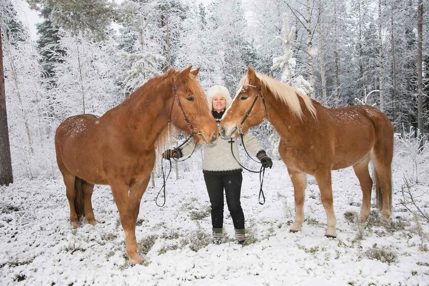 A person with two horses in a snowy forest. 1