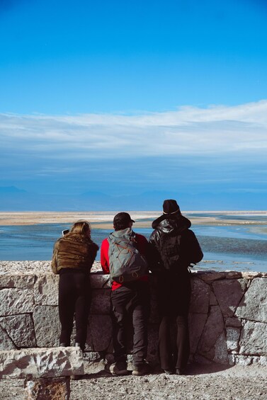 Three people standing by a stone wall overlooking a body of water. 3