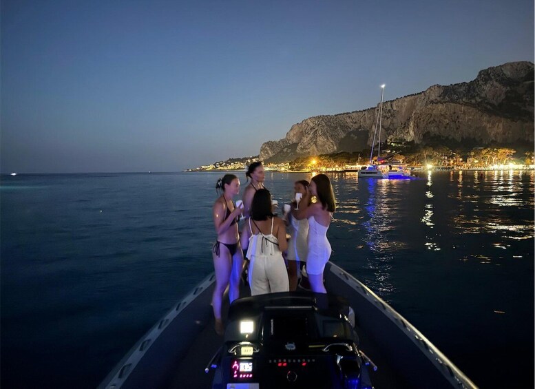 A group of people on a boat near a coastline with a rocky cliff and city lights in the background. 4
