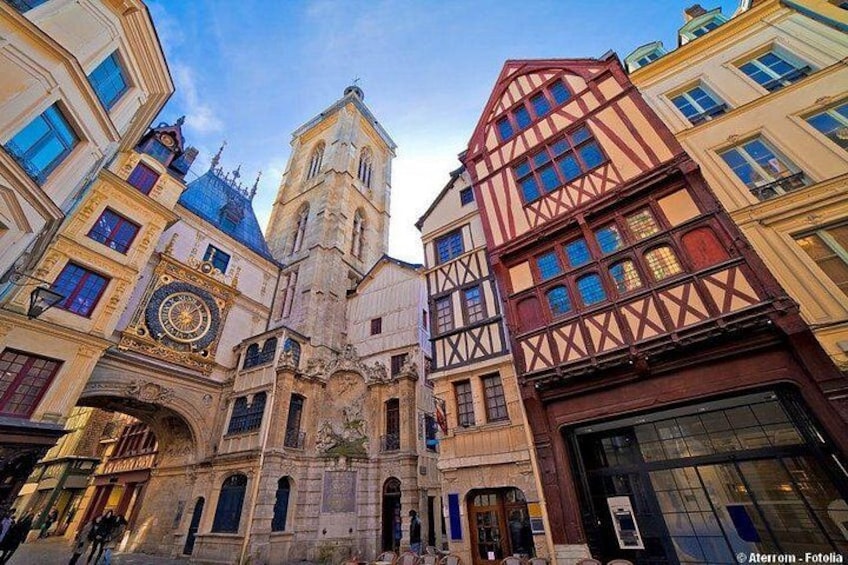 Une place historique au cœur d’une ville européenne, avec un imposant clocher d’église, des bâtiments à colombages et une grande horloge. 2