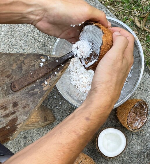 A person using a knife to cut open a coconut, with the white flesh and brown shell visible. 2