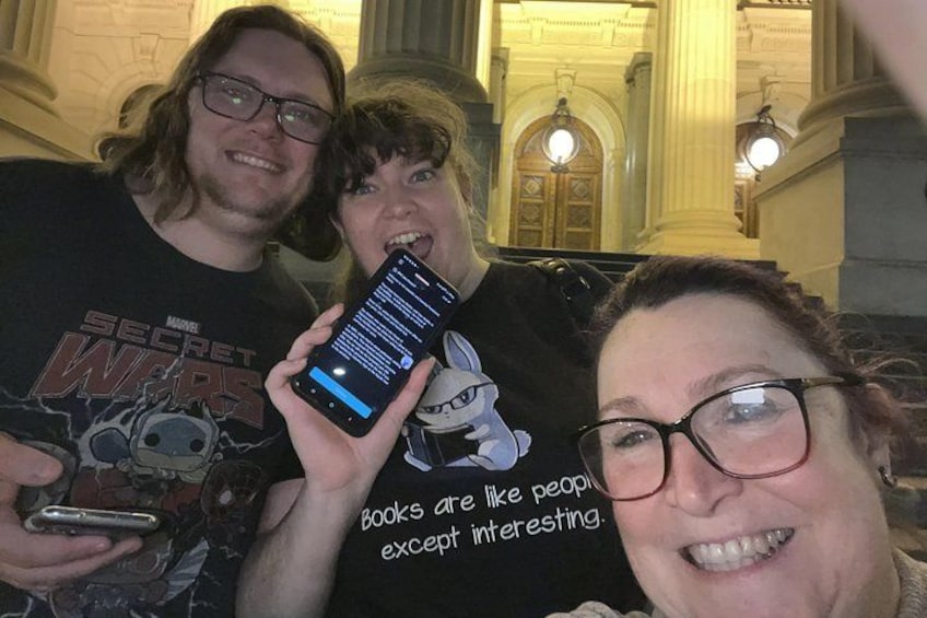 Three people in a building with columns and a chandelier. 4