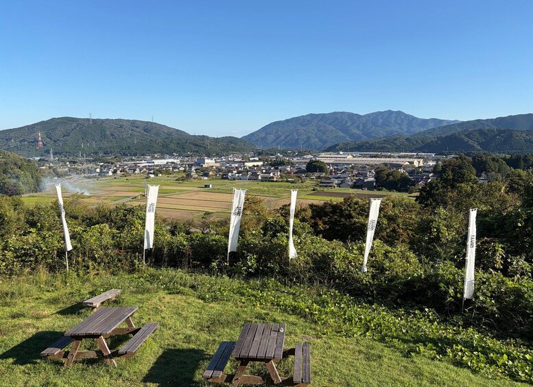 A picnic area with benches and banners in a hilly landscape with a town in the background. 4