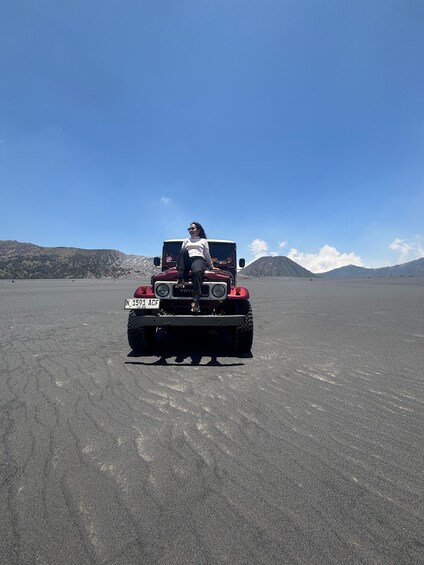 A person sitting in a red off-road vehicle with a license plate on a flat, open landscape with distant mountains. 5