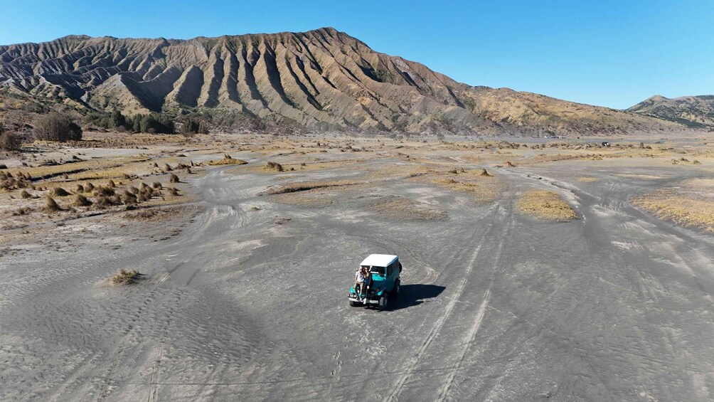 A turquoise off-road vehicle on a dirt road in a desert landscape with a large mountain in the background. 2