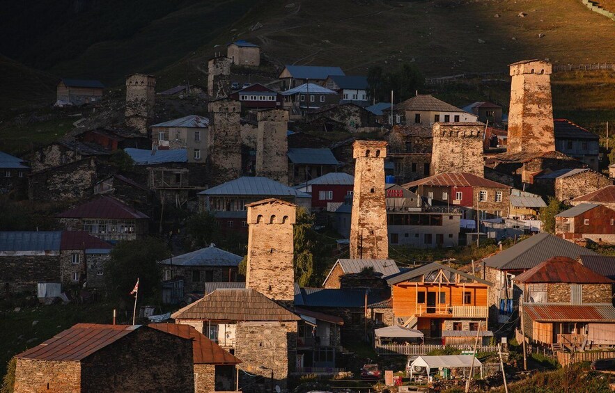 A historic town with stone buildings and towers, surrounded by hills. 2