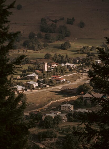 A rural landscape with scattered houses, a prominent tower, and a mix of open fields and trees. 4