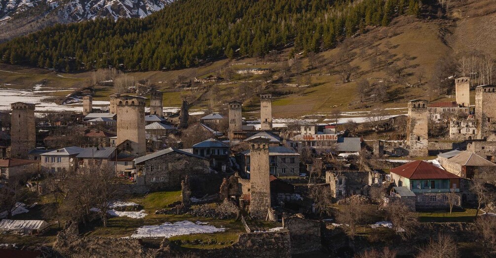A medieval town with stone buildings and towers, surrounded by mountains and snow. 3