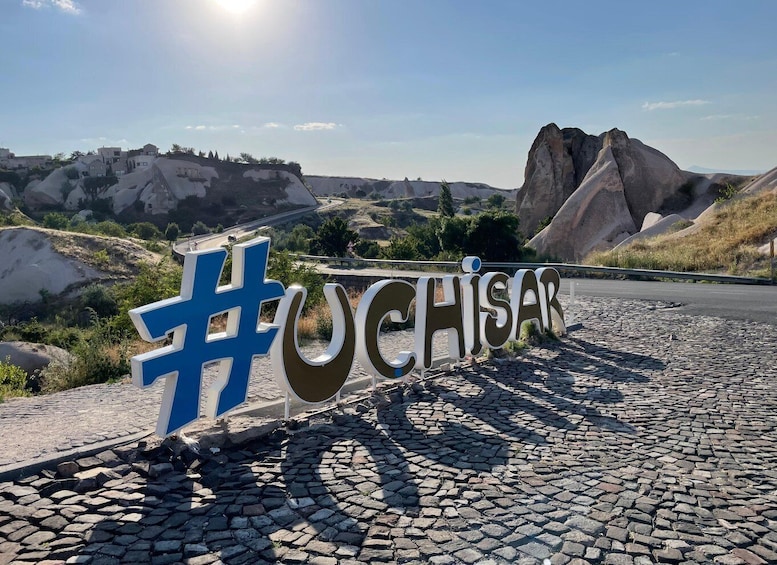 A sign with the word #UCHISAR and a mountainous landscape in the background. 1