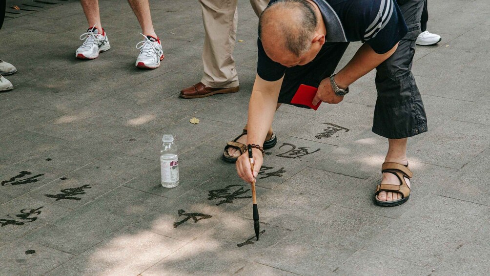 A person writing Chinese characters on a stone pavement with a brush. 4