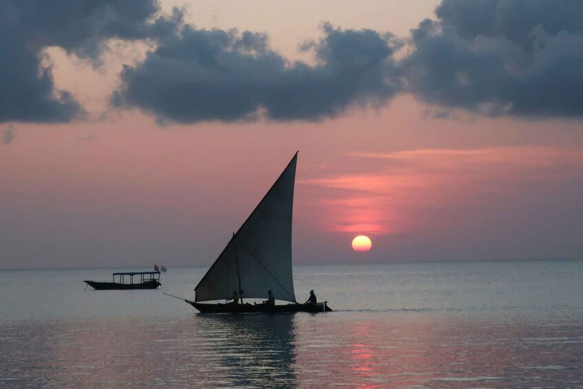 A sailboat with a large sail on calm waters at sunset. 1