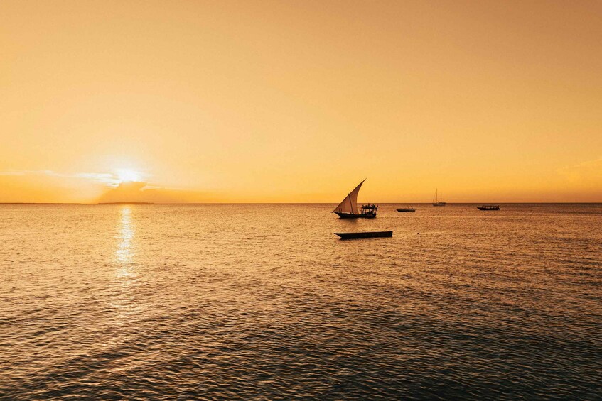A sunset over a calm sea with a sailboat and several smaller boats. 2