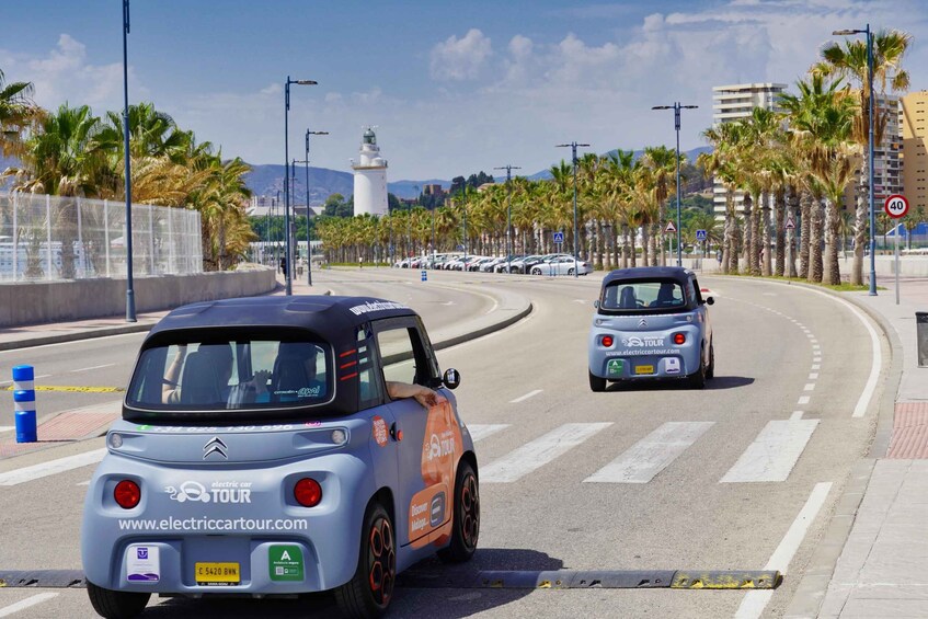 A coastal road with palm trees, a lighthouse, and parked cars. 1