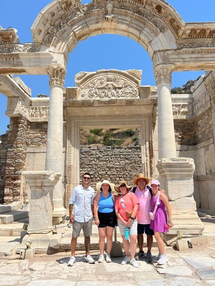 A group of people standing in front of an ancient stone archway with intricate carvings. 3