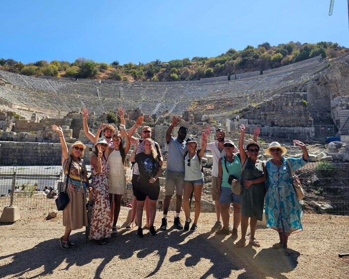 A group of people standing in front of an ancient amphitheater with ruins and a clear sky. 5