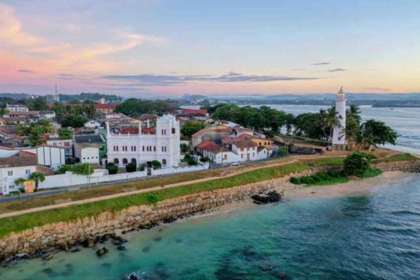 A coastal town with a prominent white church, a lighthouse, and a stone wall along the beach. 5