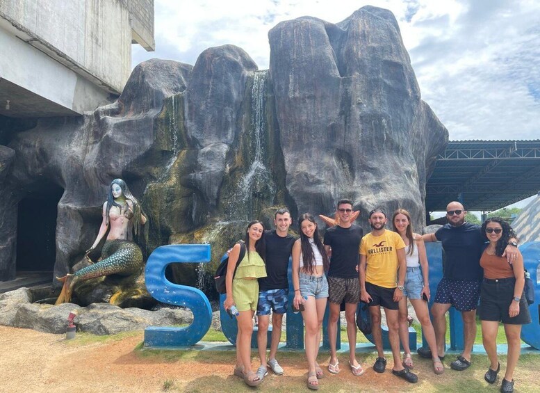A group of people posing in front of a large rock formation with a waterfall and a mermaid statue. 2