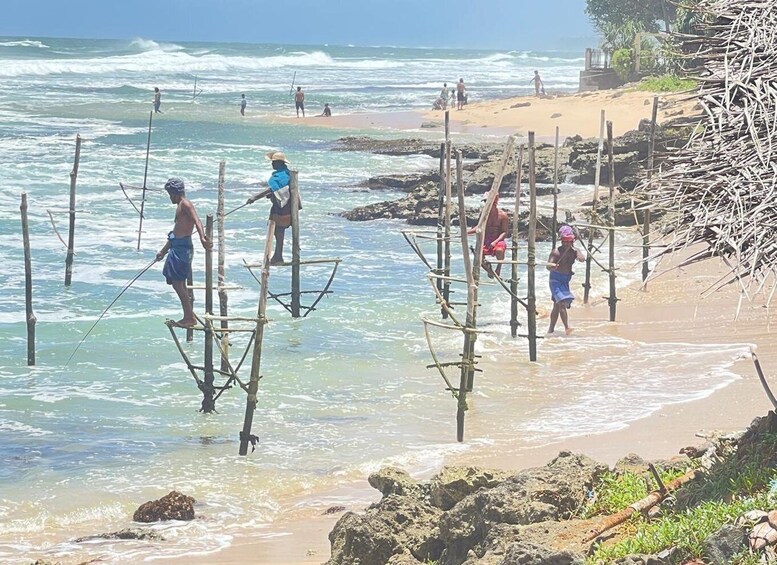 People fishing from makeshift wooden structures in shallow water near a sandy beach. 4