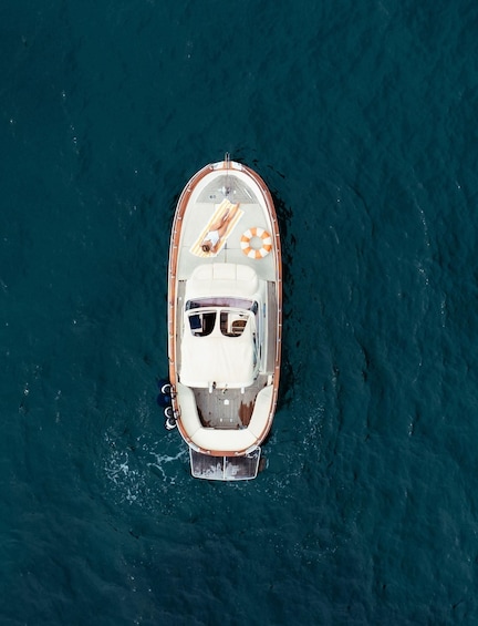 An aerial view of a small boat with a woman lying on a striped towel, a life ring, and a steering wheel. 5