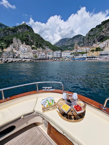 A boat with a table set with snacks and drinks, overlooking a coastal town with buildings and cliffs. 1