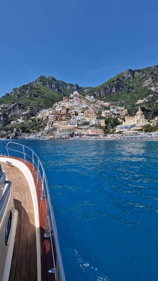 A coastal town with buildings on a hillside, a boat in the foreground, and clear blue water. 2