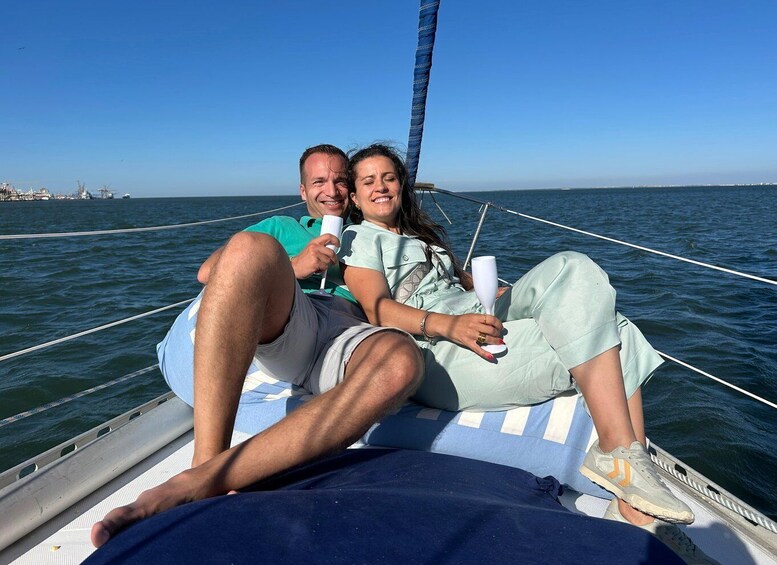 Two people on a sailboat, holding wine glasses, with a clear blue sky and calm sea in the background. 3