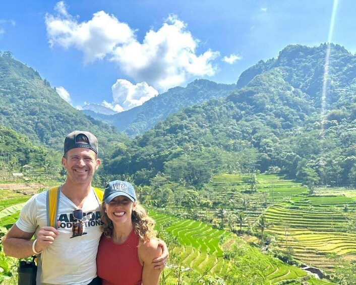 A couple standing in a terraced rice field with mountains in the background. 1