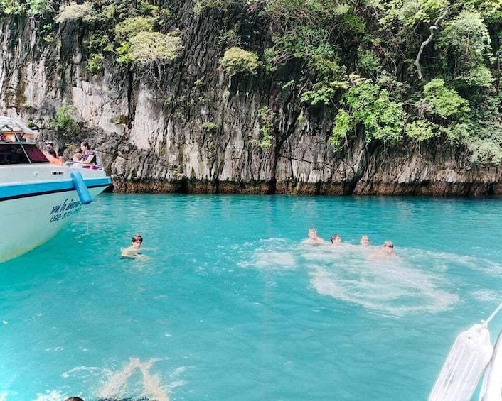 A boat with people swimming in a turquoise sea, surrounded by rocky cliffs and lush greenery. 5