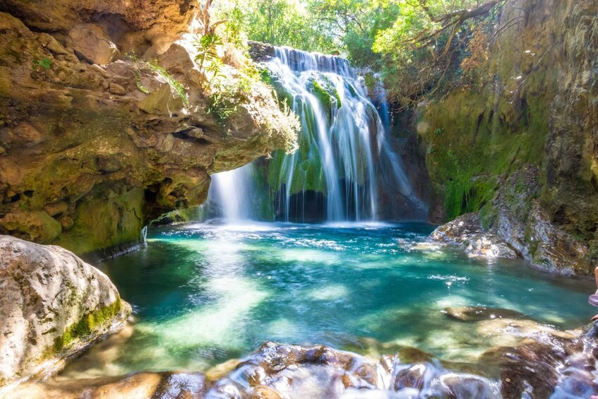 A waterfall cascading into a clear pool surrounded by rocky cliffs and lush greenery. 1