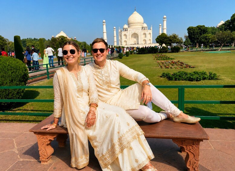 A couple sitting on a bench with the Taj Mahal in the background. 1
