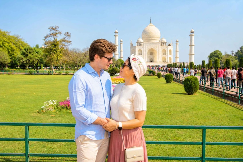 A couple standing in front of the Taj Mahal with a well-maintained garden and a crowd in the background. 1