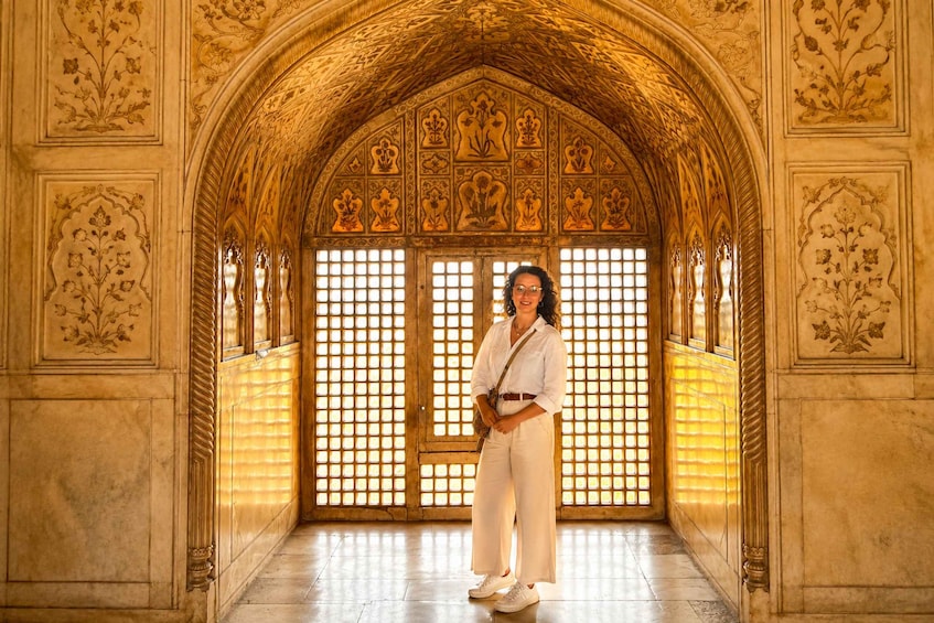 A person standing in a hallway with ornate golden arches and intricate floral patterns on the walls. 5