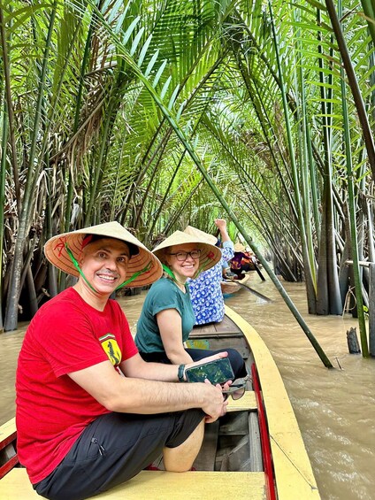 Two people in a boat navigating through a canal lined with tall, green bamboo plants. 4