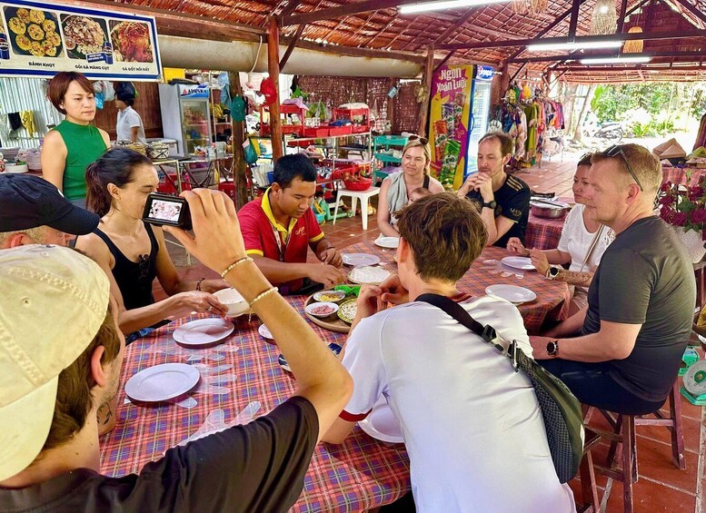 A group of people dining at an outdoor restaurant with a thatched roof. 2